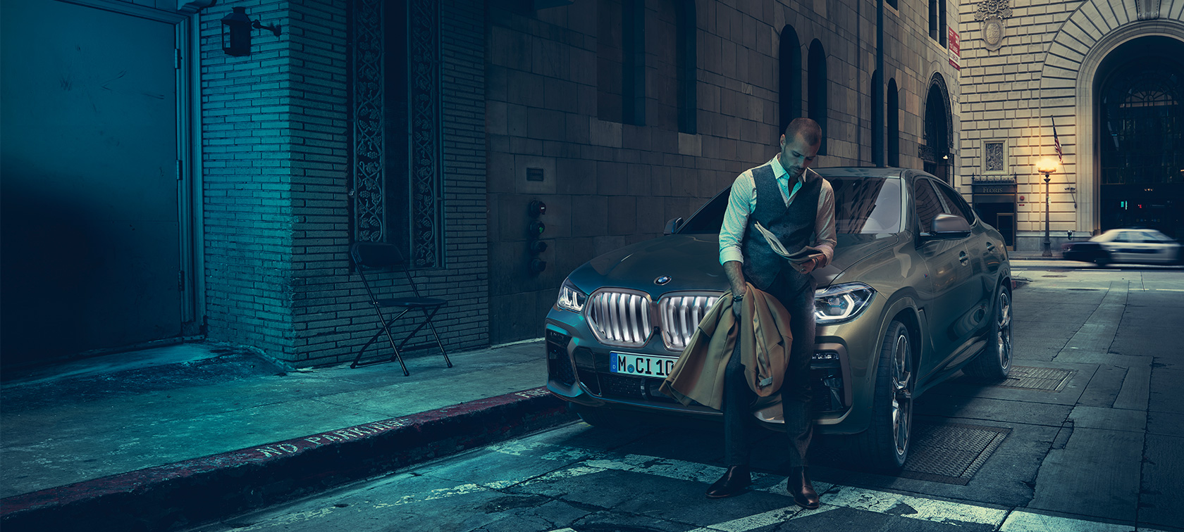 Frontale della BMW X6 M50i. Un uomo è appoggiato sul frontale della BMW X6 M50i.