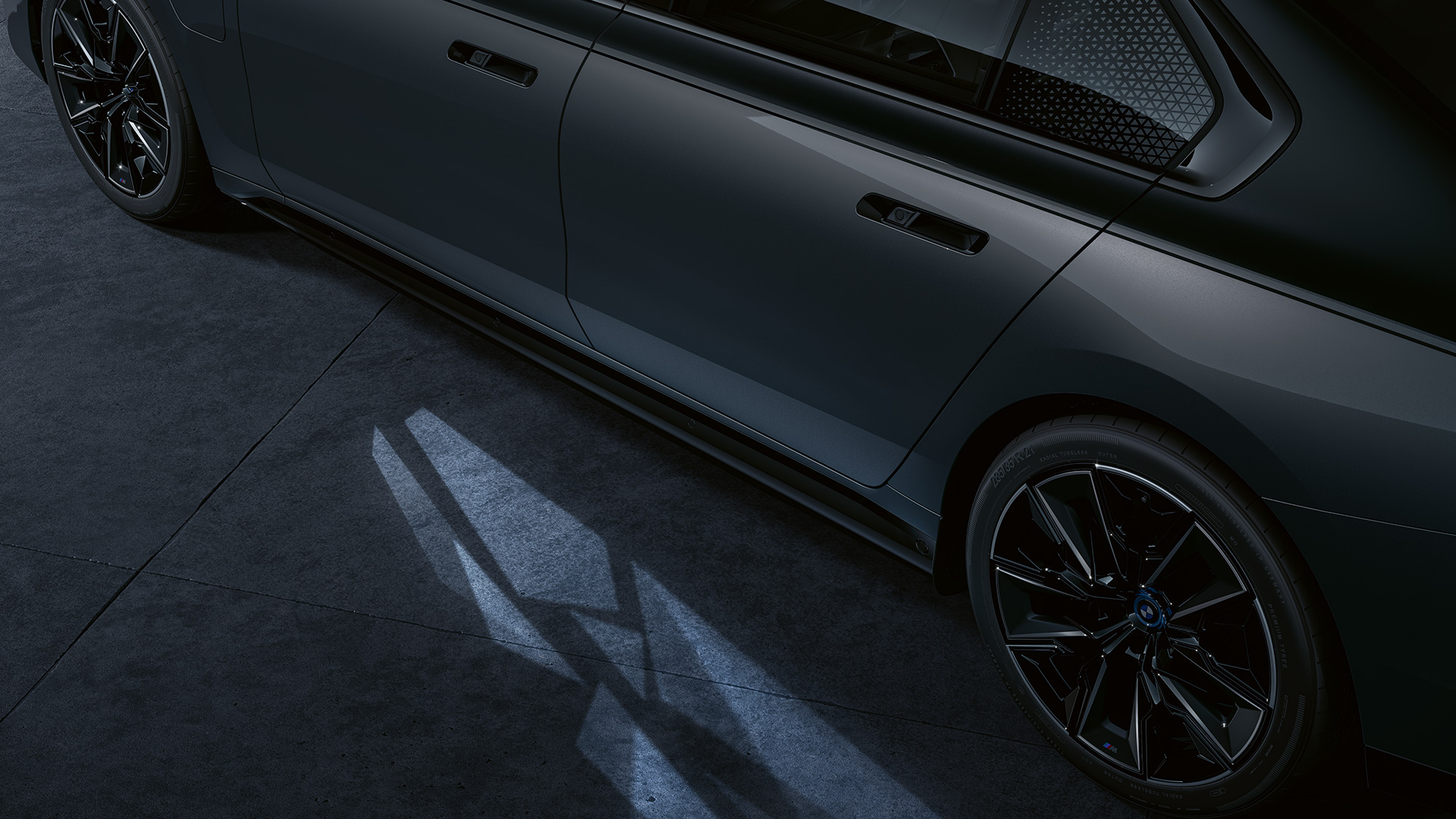 Concetto luci della BMW M760e xDrive Berlina G70 Primo piano laterale della BMW M760e xDrive Limousine G70 bicolore Sapphire Black metallizzato e BMW Individual Dravit Grey metallizzato con gioco di luci e Welcome Light Carpet attivato
