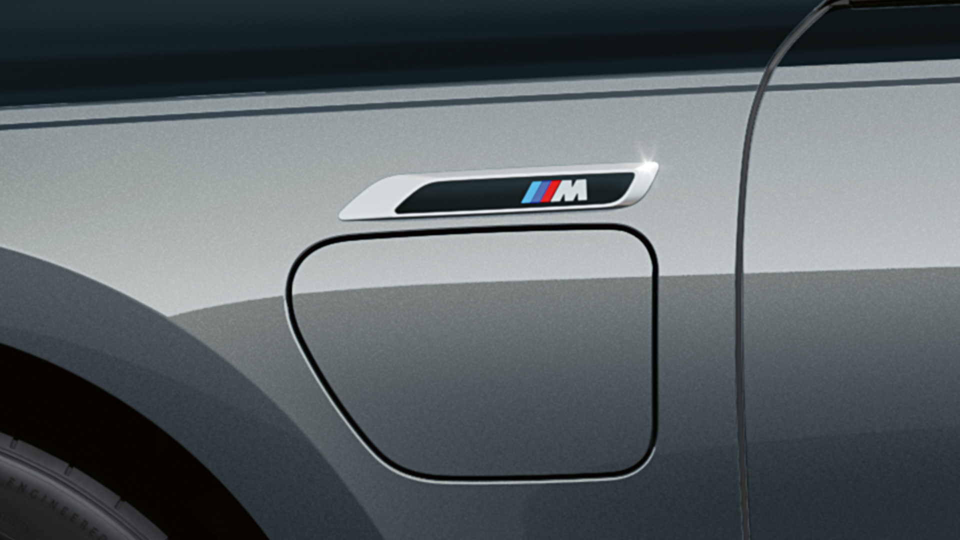 Badge M della BMW M760e xDrive Berlina G70 Primo piano della fiancata con badge M della BMW M760e xDrive Berlina G70 Pacchetto M Performance in bicolore BMW Individual Sapphire Black metallizzato e BMW Individual Dravit Grey metallizzato