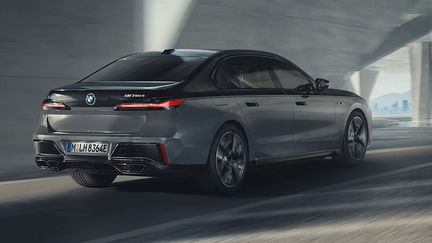 BMW M760e xDrive Berlina G70 Pacchetto M Performance Vista posteriore a tre quarti in movimento su strada della BMW M760e xDrive Berlina G70 con Pacchetto BMW M Performance, vernice bicolore BMW Individual Sapphire Black metallizzato e BMW Individual Dravit Grey metallizzato
