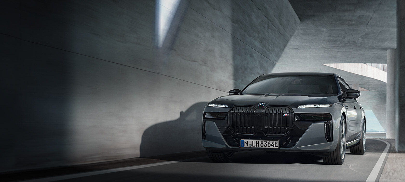 Vista frontale a tre quarti in movimento su strada della BMW M760e xDrive Berlina G70 con Pacchetto M Performance, vernice bicolore BMW Individual Sapphire Black metallizzato e BMW Individual Dravit Grey metallizzato