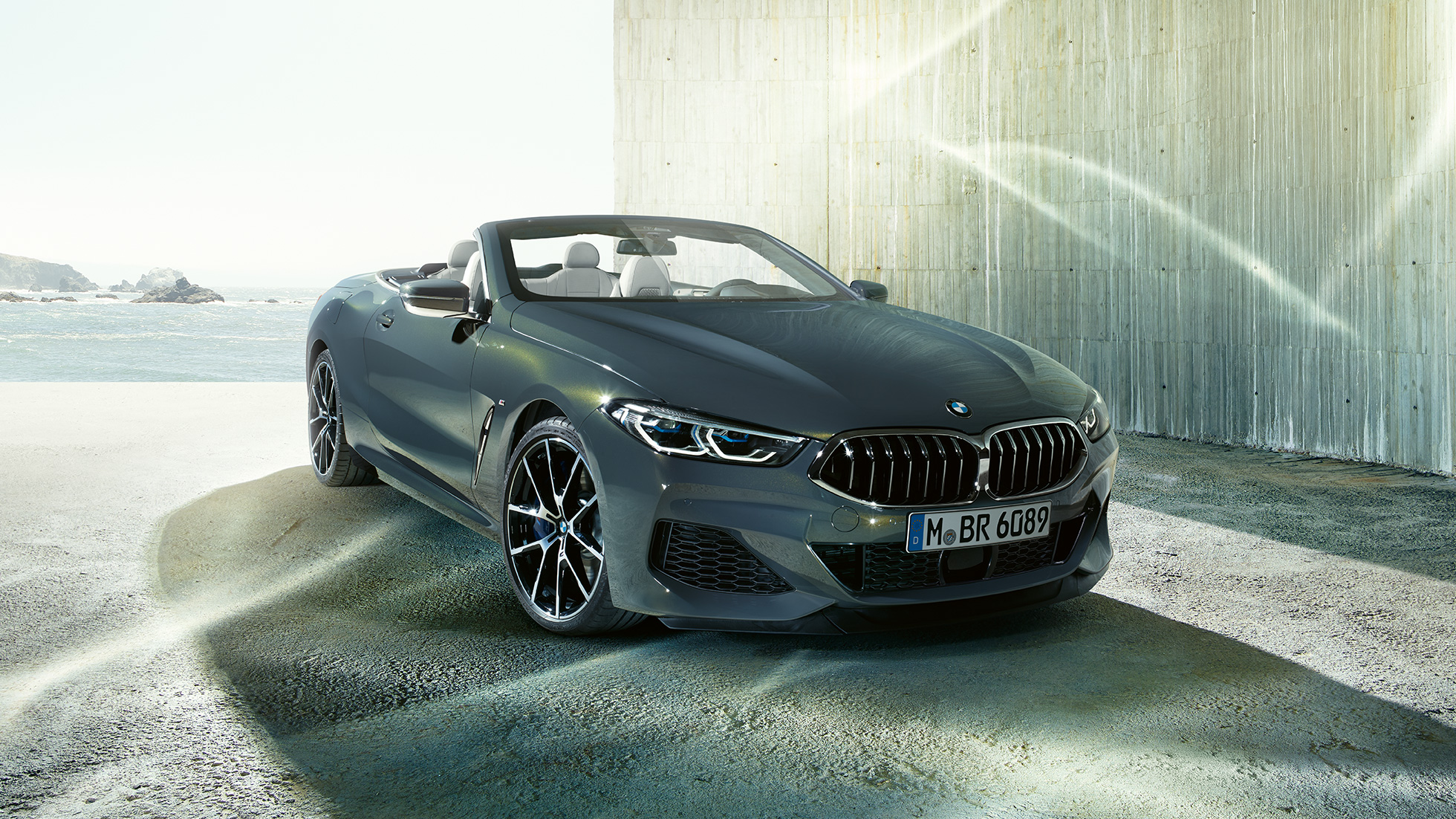 BMW M850i xDrive Cabrio, vista frontale di tre quarti G14. BMW M850i xDrive Cabrio in Dravit Grey metallizzato con capote aperta, vista frontale di tre quarti, in sosta davanti alla costa G14.