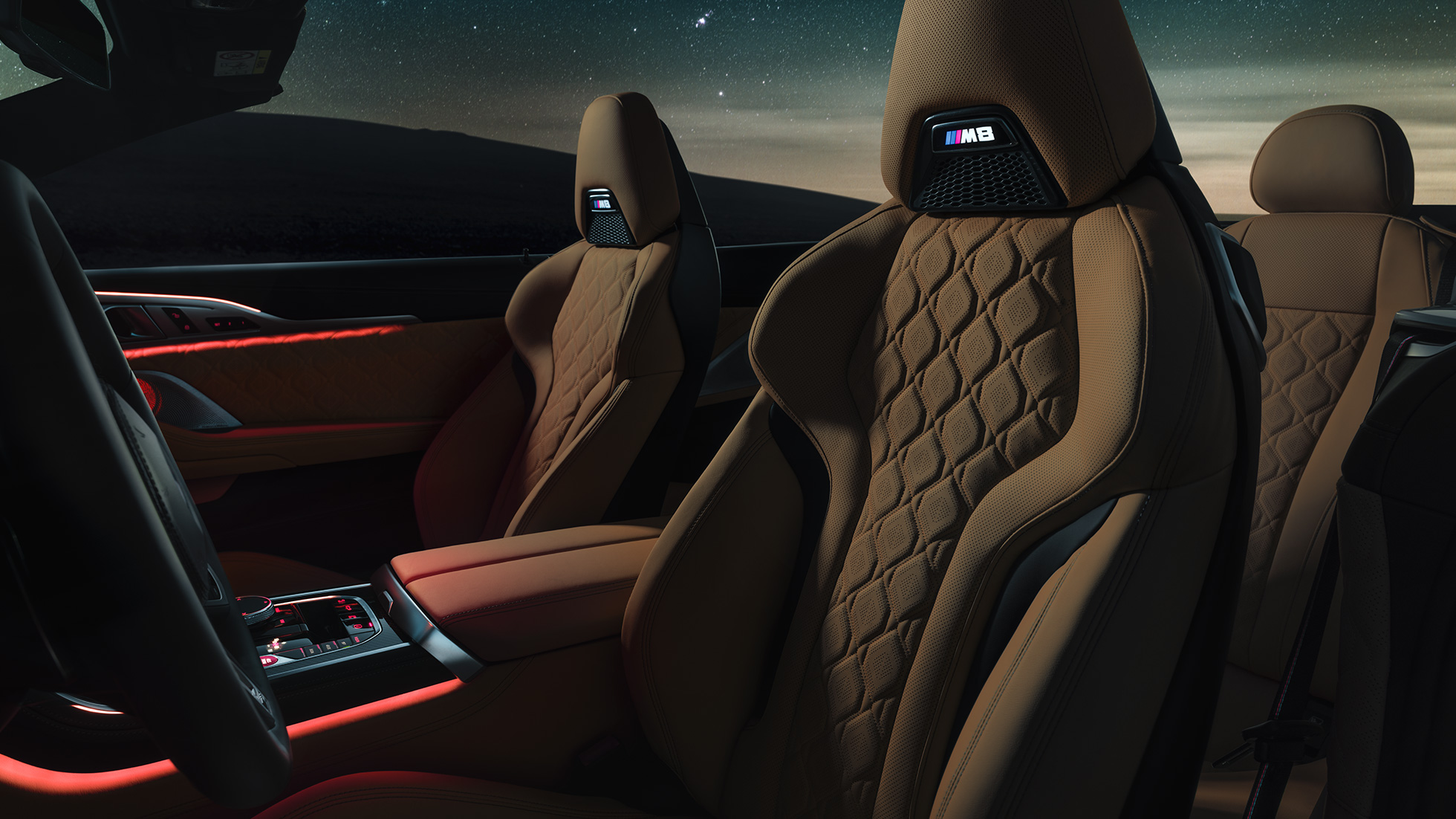 Sedili sportivi M in pelle Merino F91. BMW M8 Competition Cabrio con capote aperta sotto il cielo stellato, abitacolo con sedili sportivi M in pelle Merino e luce ambiente rossa F91.
