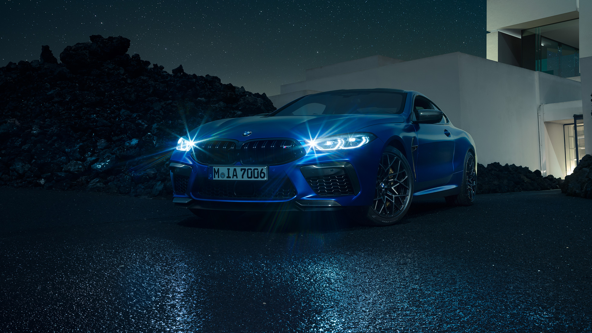 BMW M8 M Competition Coupé, vista frontale di tre quarti F92. BMW M8 Competition Coupé in Marina Bay Blue metallizzato con fari a LED accesi, vista frontale di tre quarti in sosta davanti a una villa di notte F92.