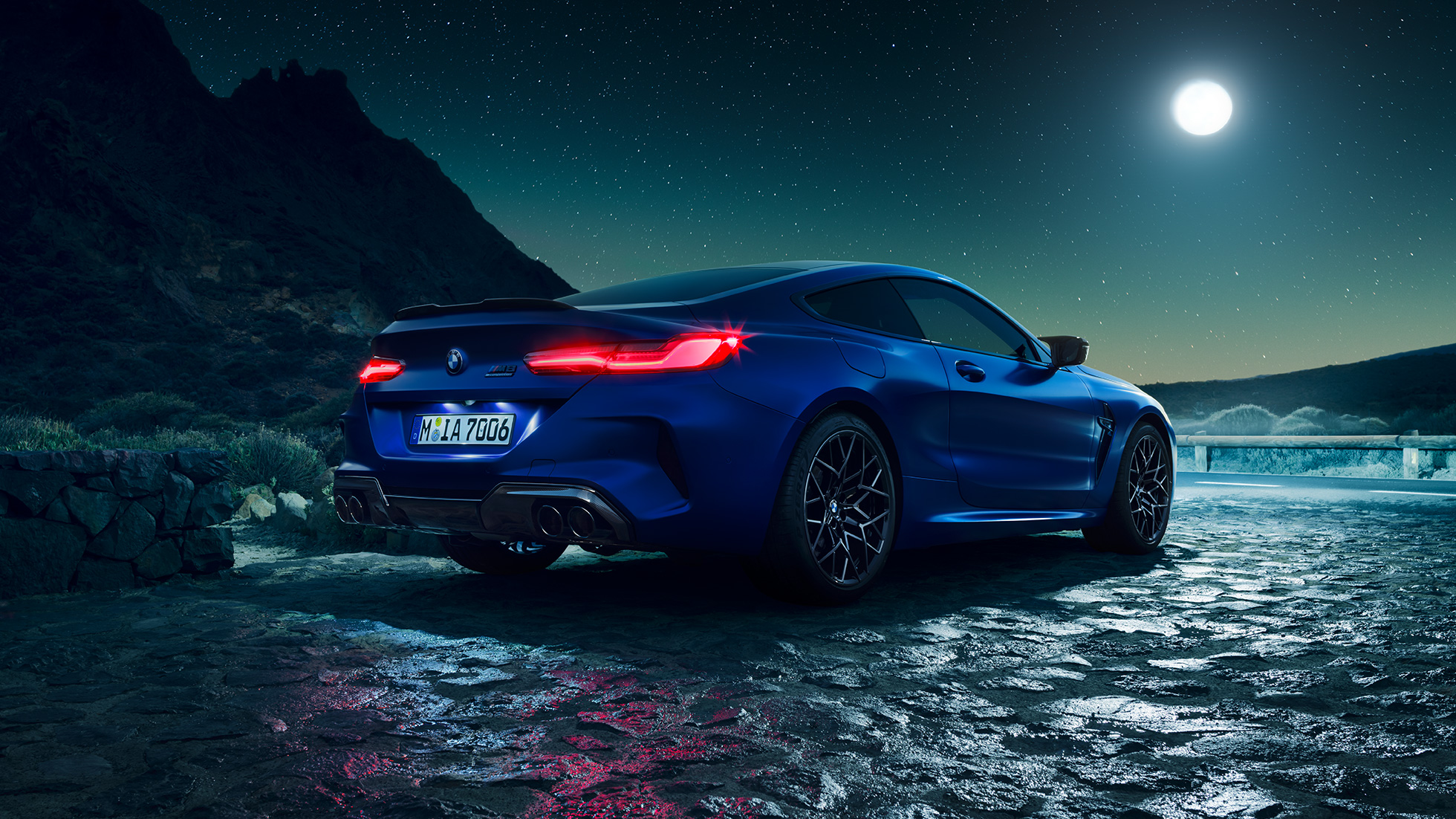BMW M8 M Coupé, vista posteriore di tre quarti F92. BMW M8 Competition Coupé in Marina Bay Blue metallizzato con gruppi ottici posteriori a LED accesi, vista posteriore di tre quarti in sosta con la luna piena F92.