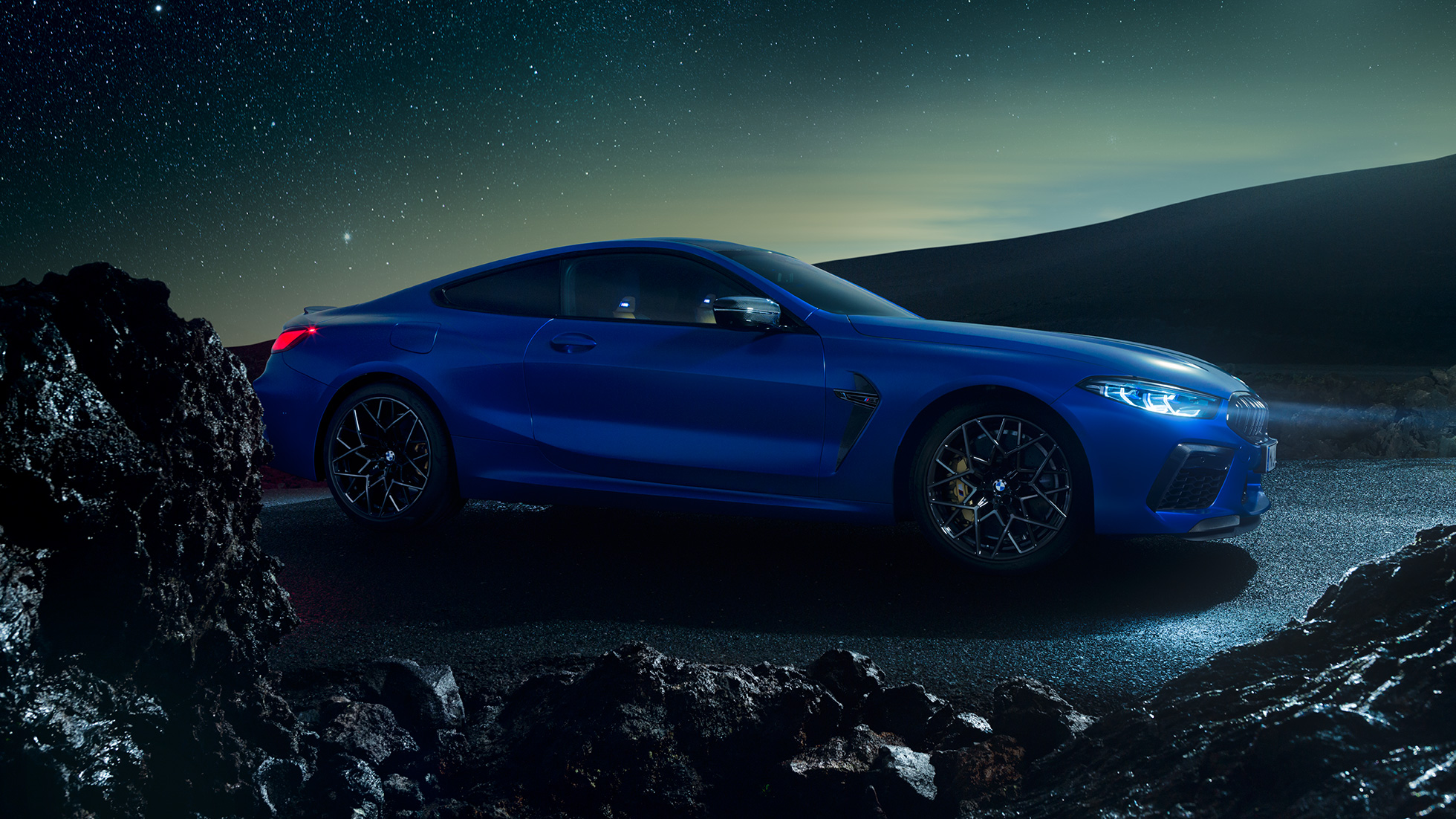 BMW M8 M Coupé, vista laterale di tre quarti F92. BMW M8 Competition Coupé in Marina Bay Blue metallizzato, vista laterale di tre quarti con auto in sosta di notte F92.