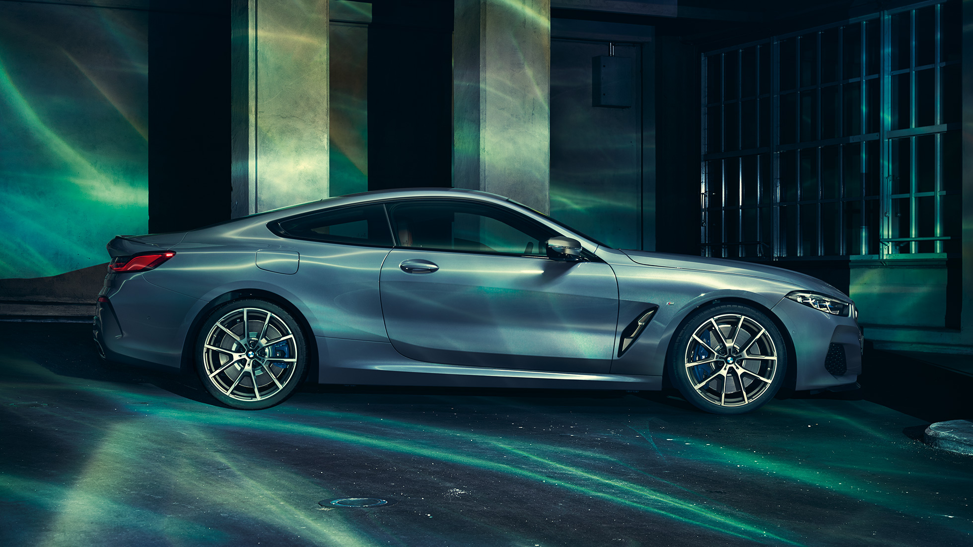 BMW M850i xDrive Coupé, vista laterale G15. BMW M850i xDrive Coupé in Barcelona Blue metallizzato, vista laterale, in sosta davanti a un edificio G15.
