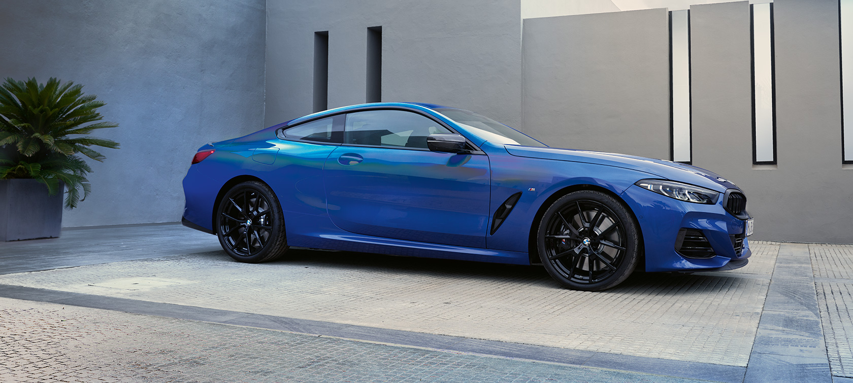 Vista laterale della BMW M850i xDrive Coupé G15 LCI Facelift 2022 BMW M850i xDrive Coupé G15 LCI Facelift 2022 M Portimao Blue metallizzato vista laterale da ferma davanti a un edificio