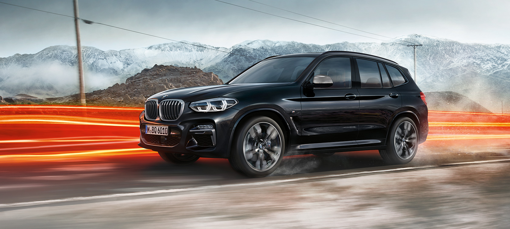 BMW X3 M40i e BMW X3 M40d, vista laterale. G01 BMW X3 M40i e BMW X3 M40d in Sapphire Black metallizzato, in movimento, esterni, vista laterale su sfondo collinare con strisce di luce. G01