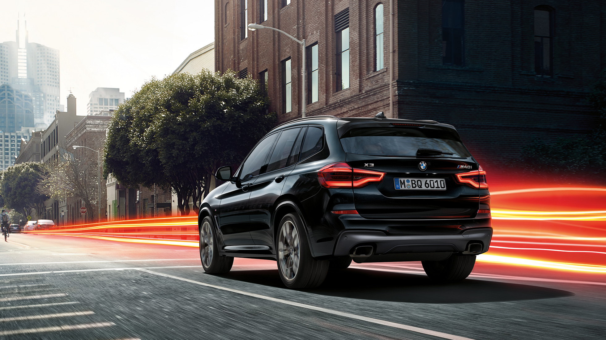 Nuova BMW X3 M40i, vista posteriore a tre quarti. G01 Nuova BMW X3 M40i in Sapphire Black metallizzato, in movimento, esterni, vista posteriore a tre quarti su sfondo urbano con strisce di luce. G01