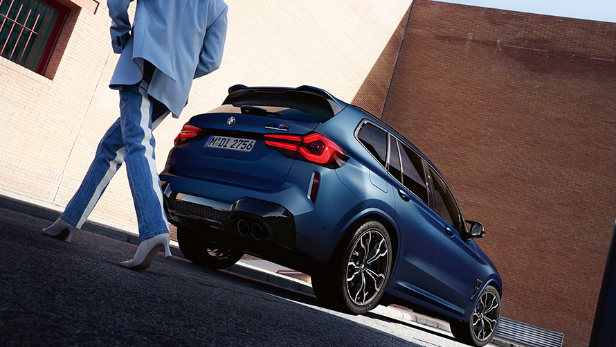 BMW X3 M Competition F97 LCI 2021 Vista posteriore a tre quarti con prospettiva dal basso con modella BMW X3 M Competition F97 LCI Facelift 2021 Frozen Marina Bay Blue metallizzato Vista posteriore a tre quarti prospettiva dal basso e modella