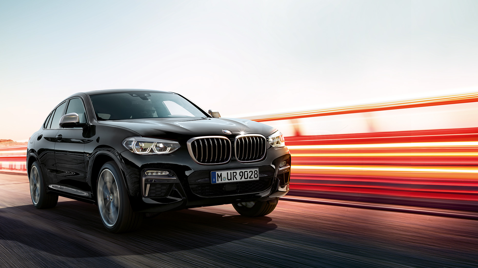 BMW X4 M40i, vista posteriore a tre quarti G02. BMW X4 M40i in Sapphire Black metallizzato, in movimento, esterni, vista posteriore a tre quarti con strisce di luce G02.