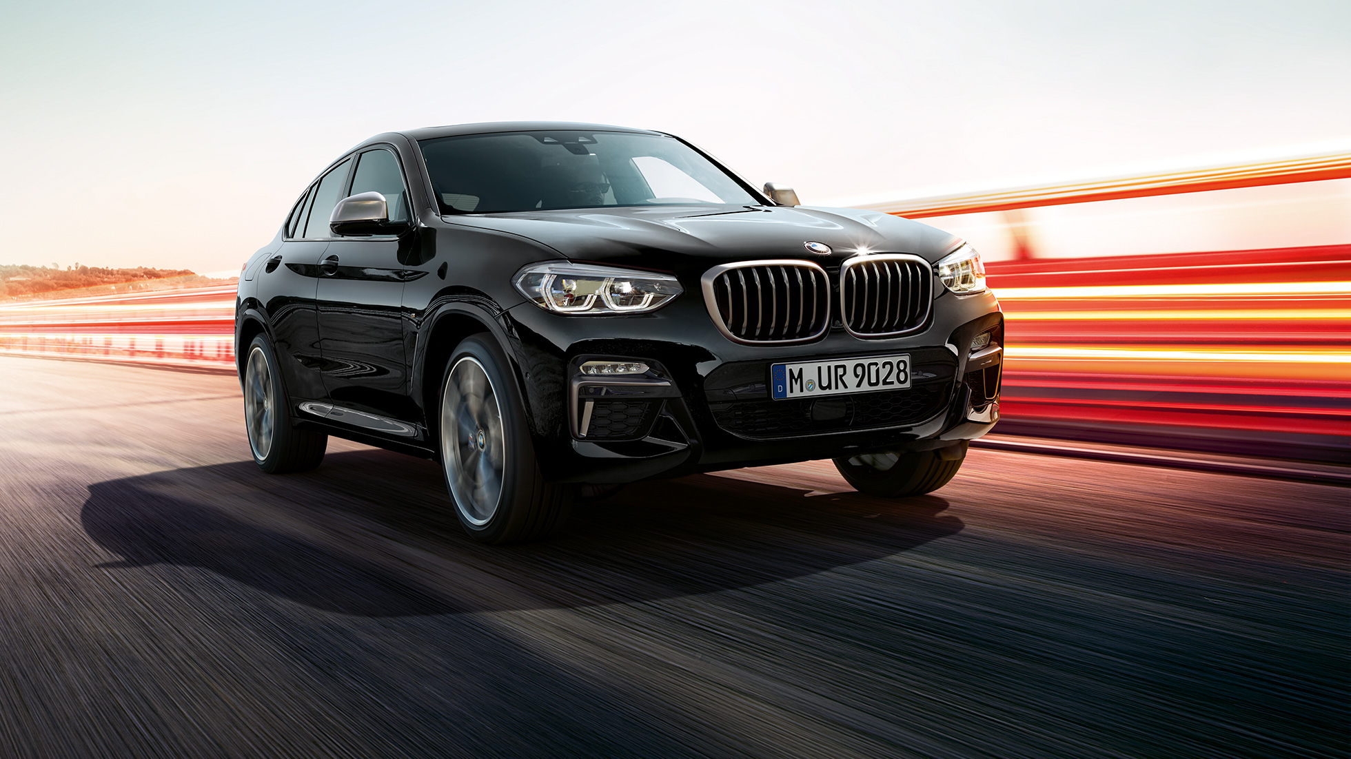 BMW X4 M40i e BMW X4 M40d, vista anteriore a tre quarti G02. BMW X4 M40i e BMW X4 M40d in Sapphire Black metallizzato, esterni, vista anteriore a tre quarti sinistra con strisce di luce G02.