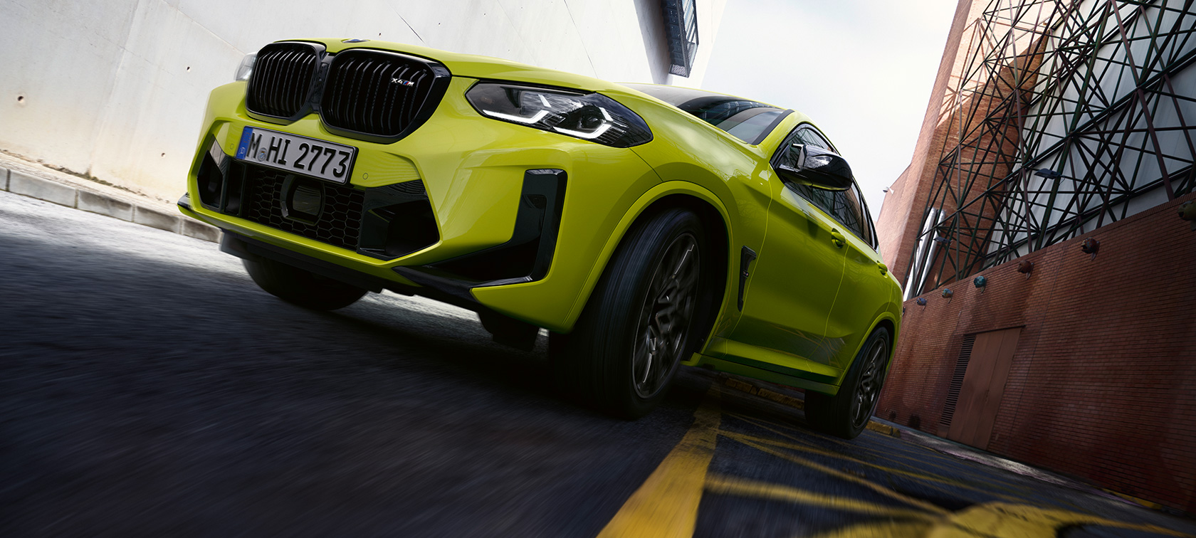 Vista anteriore a tre quarti dal basso della BMW X4 M Competition F98 LCI 2021 BMW X4 M Competition F98 LCI Facelift 2021 Sao Paulo Yellow Vista anteriore a tre quarti dal basso in movimento tra case