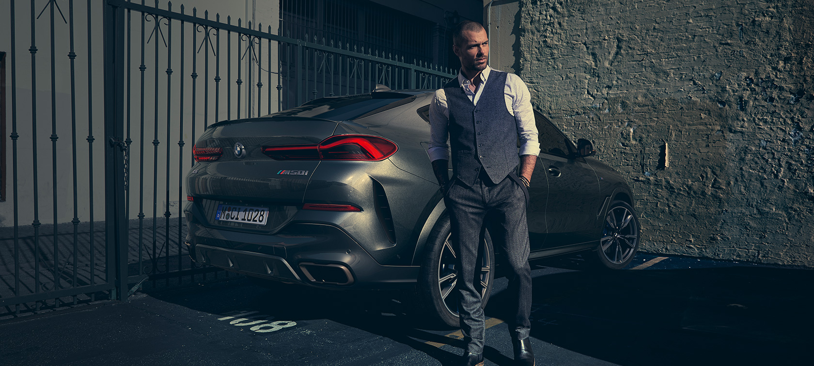 BMW X6 M50i in vista posteriore a tre quarti G06 Un uomo accanto alla BMW X6 M50i G06 2018 SUV in vista posteriore a tre quarti
