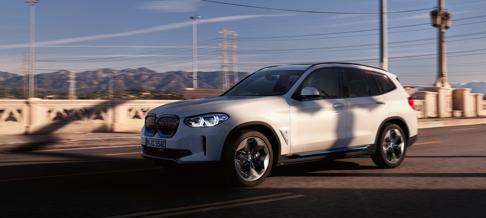BMW iX3 G08 vista anteriore a tre quarti in movimento su strada BMW iX3 G08 2020 Mineral White metallizzato vista anteriore a tre quarti in strada