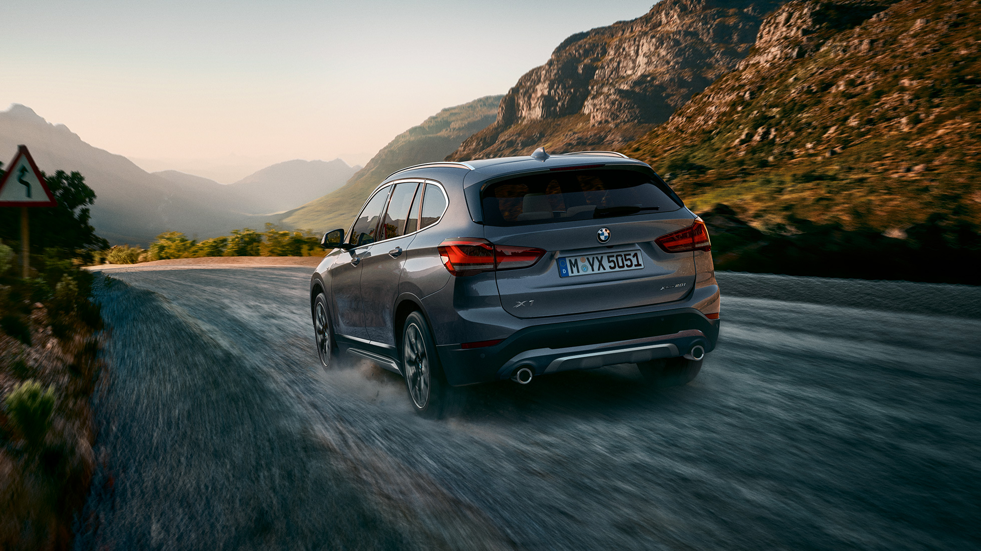 BMW X1, vista posteriore a tre quarti. BMW X1, vista posteriore a tre quarti in movimento in un paesaggio montano.