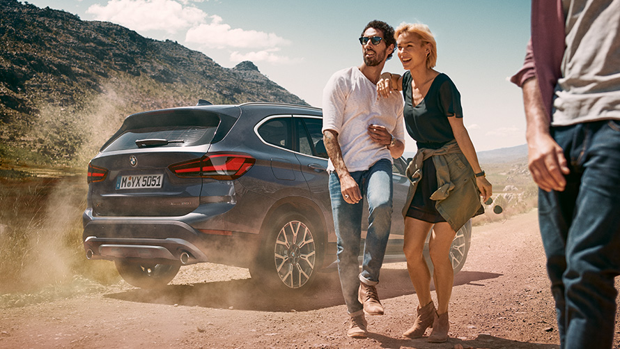 BMW X1 F48 LCI Storm Bay Vista posteriore a tre quarti BMW X1 F48 LCI Storm Bay Vista posteriore a tre quarti in un paesaggio con persone davanti