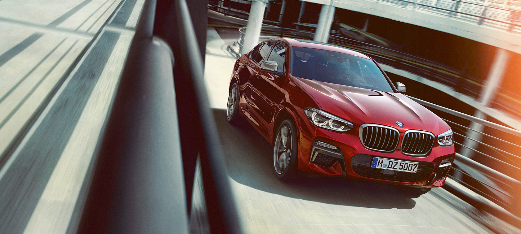 BMW X4 in movimento in un autosilo G02 BMW X4 G02 2018 Flamenco Red brilliant effect vista laterale a tre quarti in movimento all’interno di un autosilo