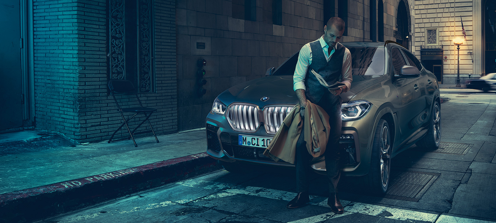 Un uomo è appoggiato alla BMW X6 G06. Vista laterale di un uomo appoggiato alla BMW X6 in ambiente urbano G06.