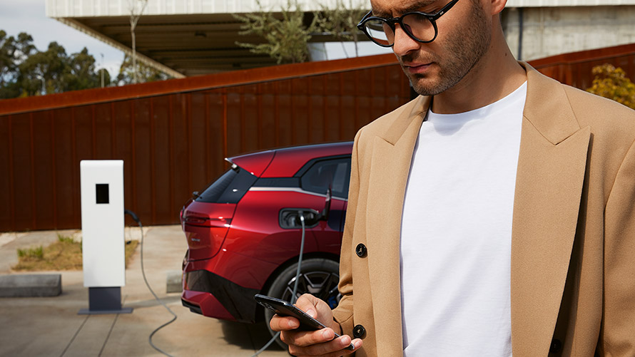 Un uomo con uno smartphone davanti a una BMW iX presso una stazione di ricarica Un uomo con uno smartphone davanti a una BMW iX presso una stazione di ricarica