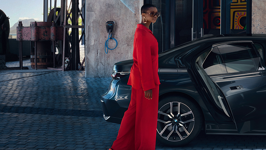 BMW Destination Charging BMW davanti a un hotel BMW Destination Charging Una donna in piedi davanti a una BMW con edificio sullo sfondo.