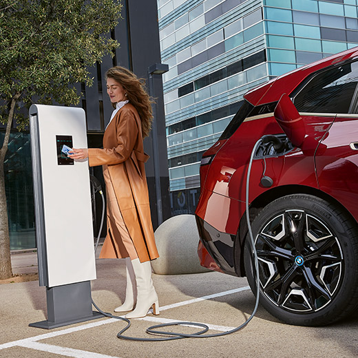 BMW iX i20 vicina alla colonnina di ricarica BMW iX i20 con una donna vicino alla colonnina di ricarica con BMW Charging Card