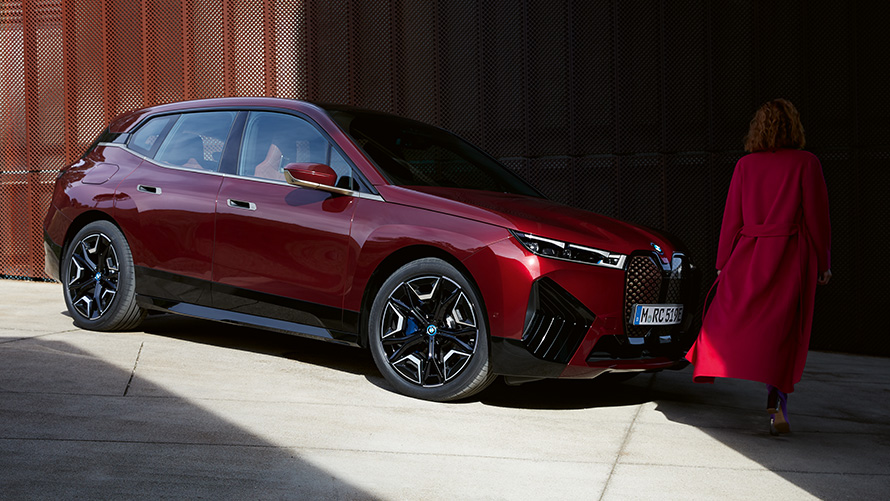 BMW Digital Key Plus BMW iX, vista frontale a tre quarti con donna BMW Digital Key Plus BMW iX, vista frontale a tre quarti con donna con cappotto rosso