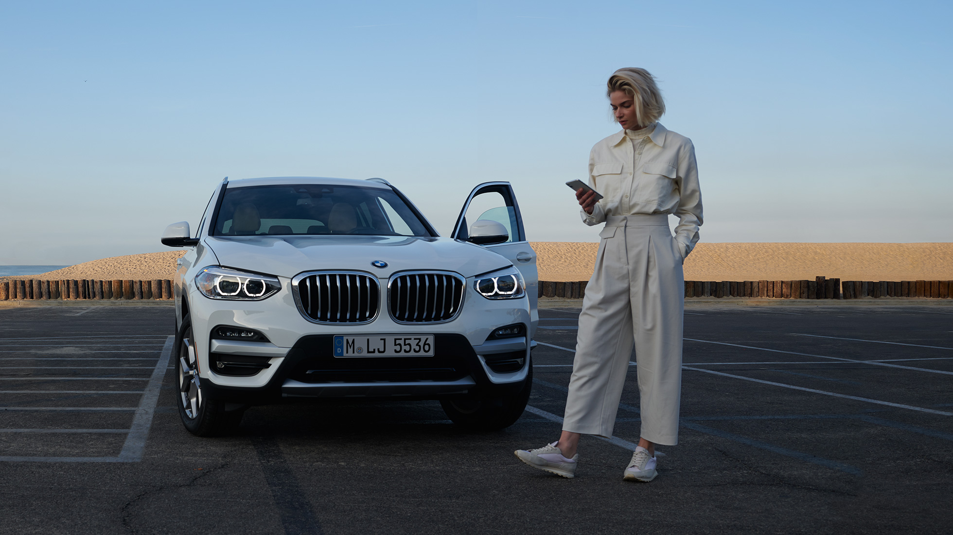 Una donna utilizza l’app My BMW sul proprio smartphone Una donna utilizza l’app My BMW di BMW ConnectedDrive sul proprio smartphone davanti alla BMW X5