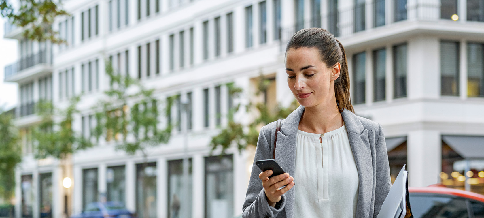 Donna davanti a un edificio con sguardo sul proprio smartphone Remote Software Upgrade donna davanti a un edificio con sguardo sul proprio smartphone