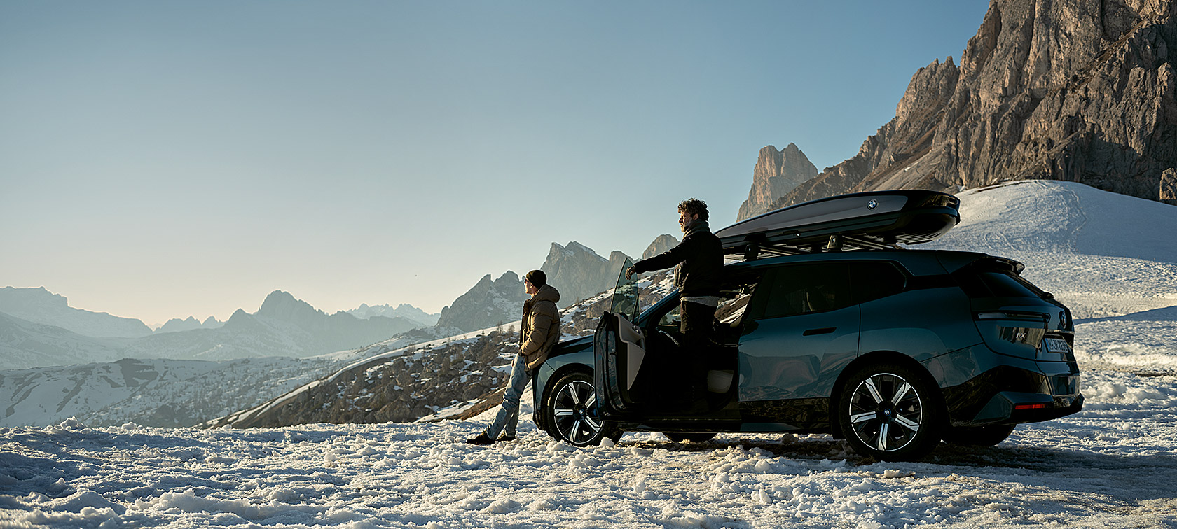 Accessori originali BMW e BMW Service per l'autunno e l'inverno Uomini con BMW iX con paesaggio innevato