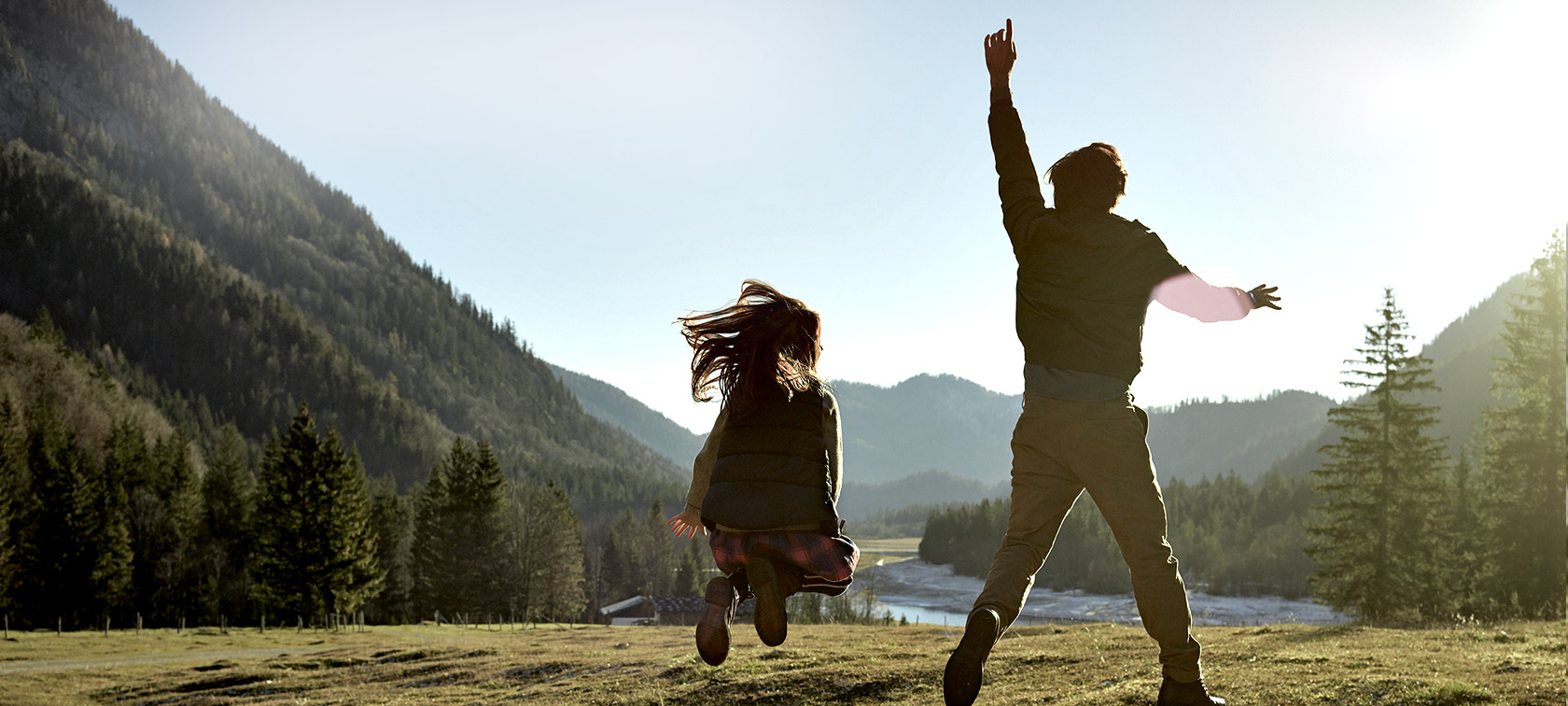 Uomo e bambina sul prato di una valle montana, vista posteriore Uomo e bambina che saltano sul prato di una valle montana, vista posteriore