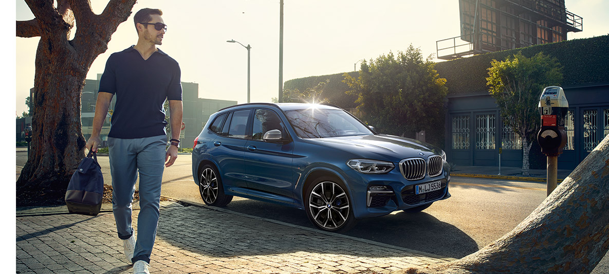 Uomo con occhiali da sole davanti a una BMW blu Uomo con occhiali da sole davanti a una BMW blu