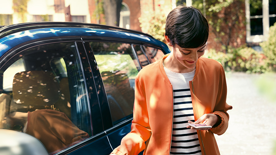 Offerte BMW per l'estate BMW Teleservices Offerte BMW per l’estate BMW Teleservices Donna con smartphone davanti a una BMW