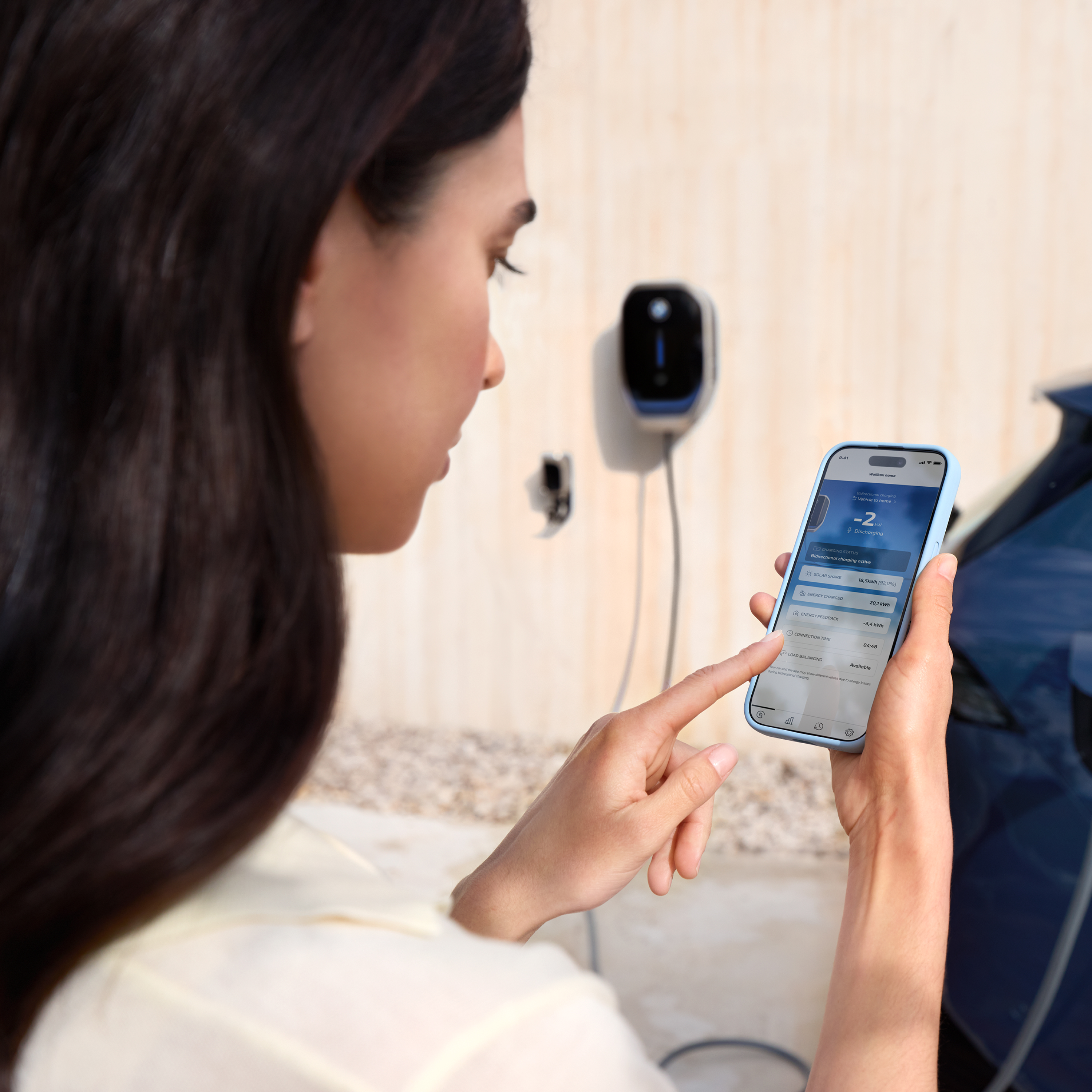 Una donna guarda il suo smartphone con una BMW Wallbox sullo sfondo
