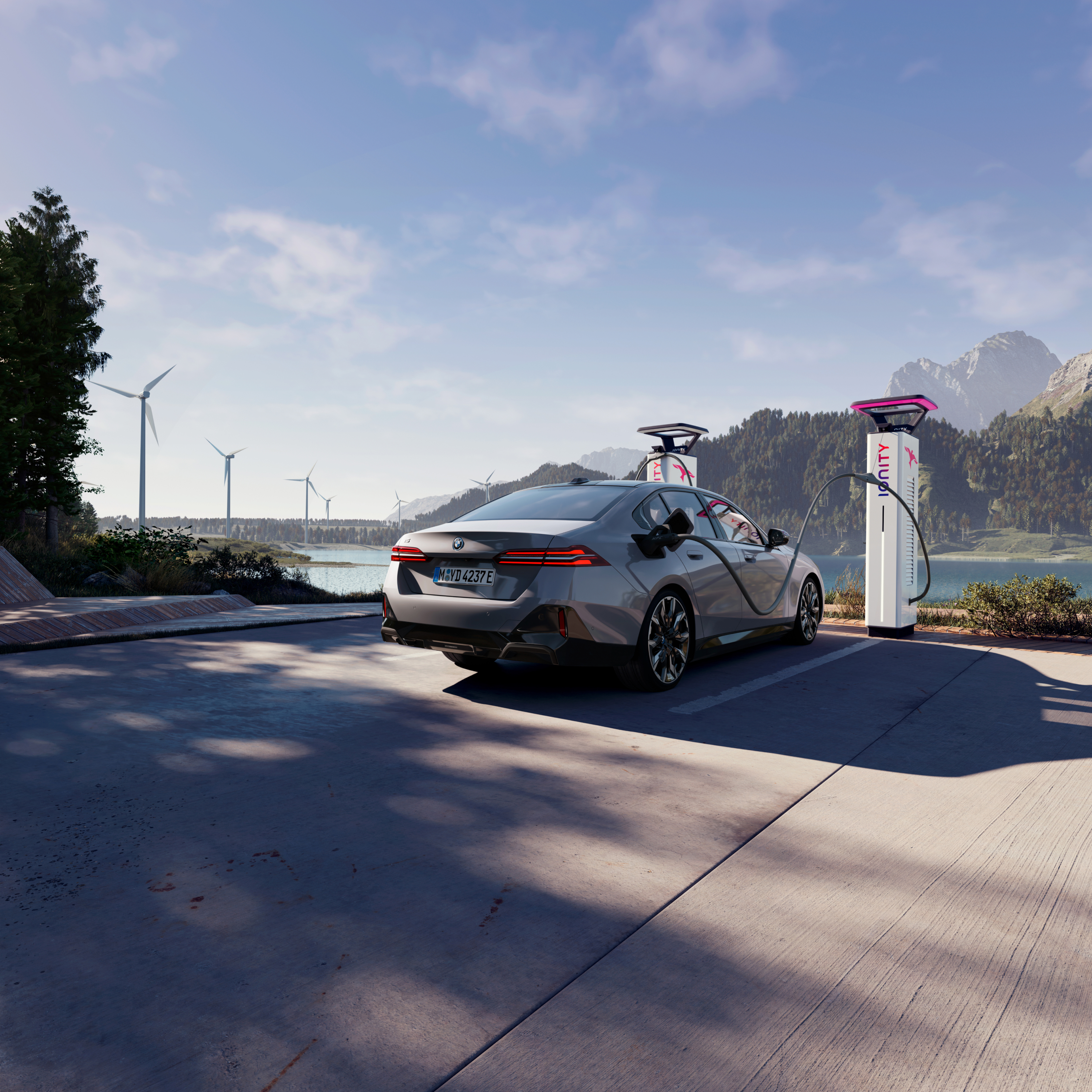 BMW in carica presso una colonnina di ricarica con vista sull'acqua, sulle montagne e sulle turbine eoliche