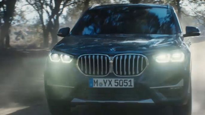 BMW X1, vista anteriore a tre quarti. BMW X1, vista anteriore a tre quarti in movimento in un paesaggio naturale.